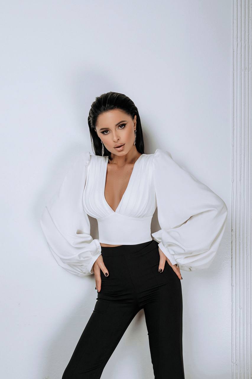Woman wearing a white blouse and black pants against a white wall
