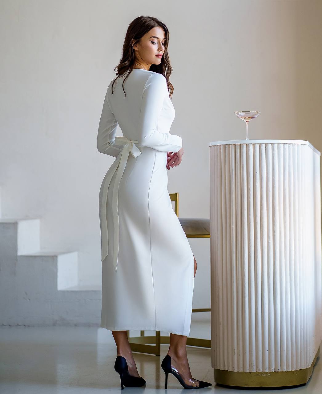 Woman in a white dress standing next to a decorative column in an elegant interior setting.