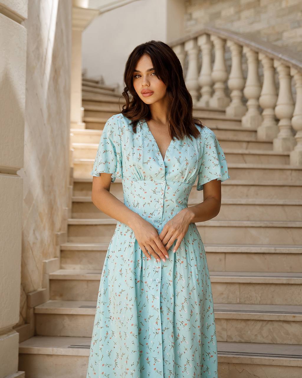 Woman in a light blue floral dress standing on a staircase with marble walls.