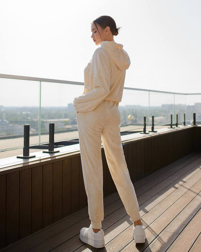 Person wearing a beige tracksuit standing on a rooftop with a cityscape view.