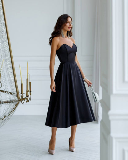 Woman in a black strapless dress standing in a stylish interior setting.