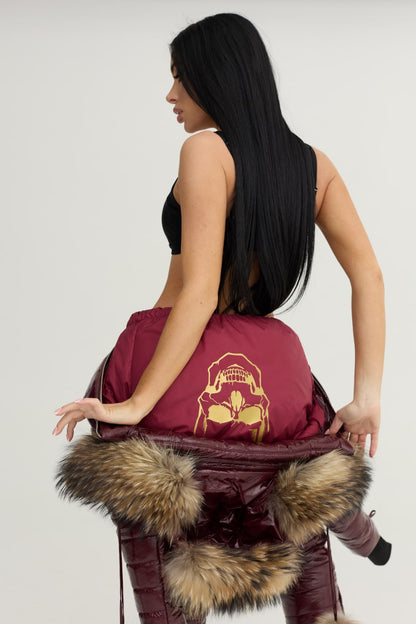 Person wearing a maroon jacket with fur trim and a gold graphic design on a plain background