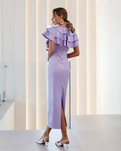 Woman wearing a lavender dress with ruffled shoulders in a modern indoor setting.