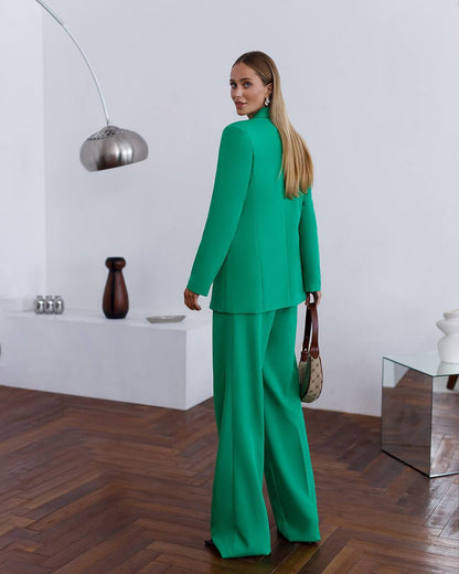 Woman in a green suit standing in a modern room with wooden flooring and white walls.