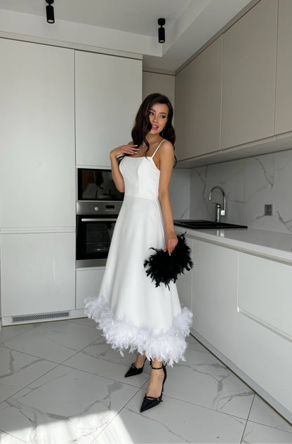Woman in a white dress with black feathers standing in a modern kitchen.