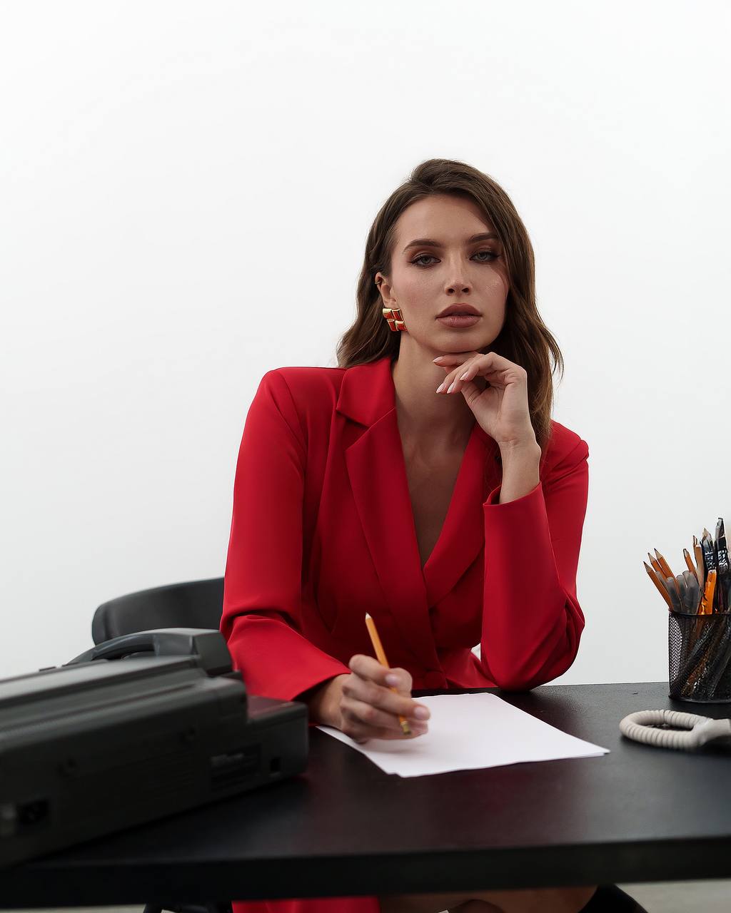 Woman in a red blazer sitting at a desk with a white background