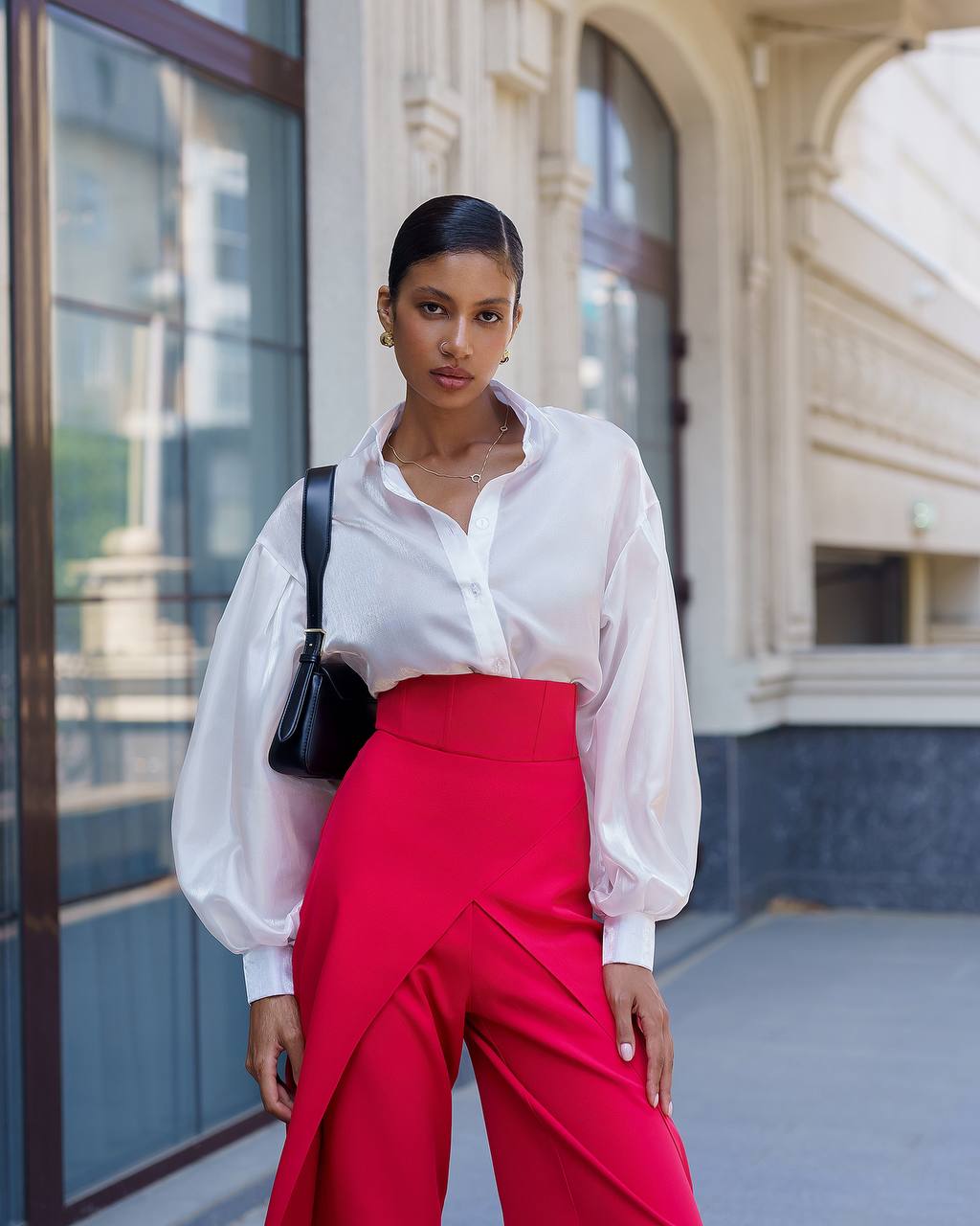 Woman wearing a white blouse and red pants standing in front of a building.