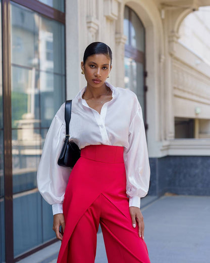 Woman wearing a white blouse and red pants standing in front of a building.
