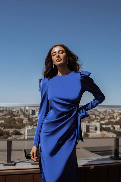 Woman in a blue dress standing on a rooftop with a cityscape in the background