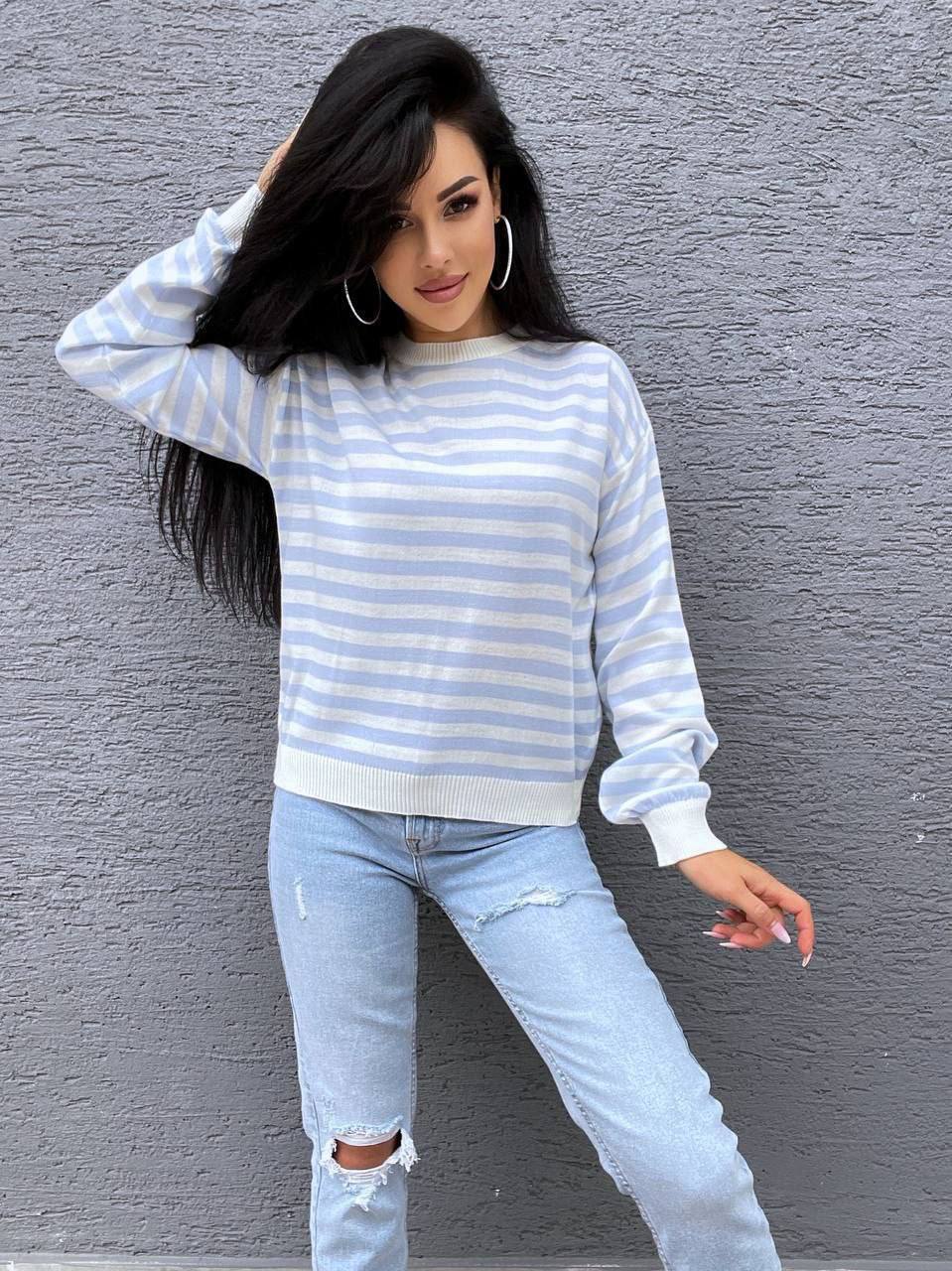 Woman wearing a striped sweater and ripped jeans against a gray wall