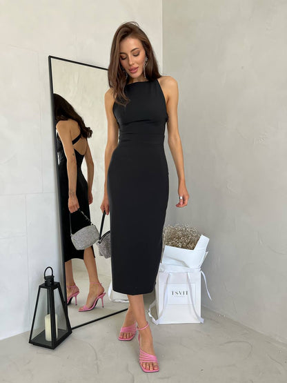 Woman in a black sleeveless dress standing in front of a mirror, with a white bag and lantern on the floor.