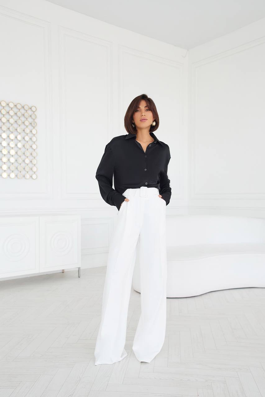 Person wearing a black shirt and white pants in a minimalistic room.