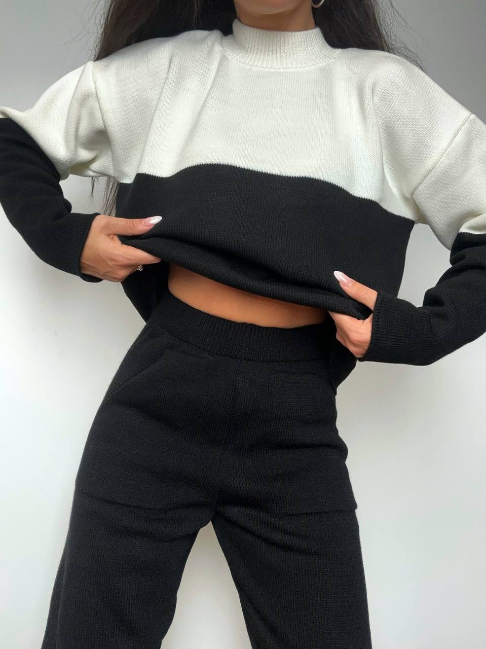 Person wearing a black and white sweater with black pants against a plain background