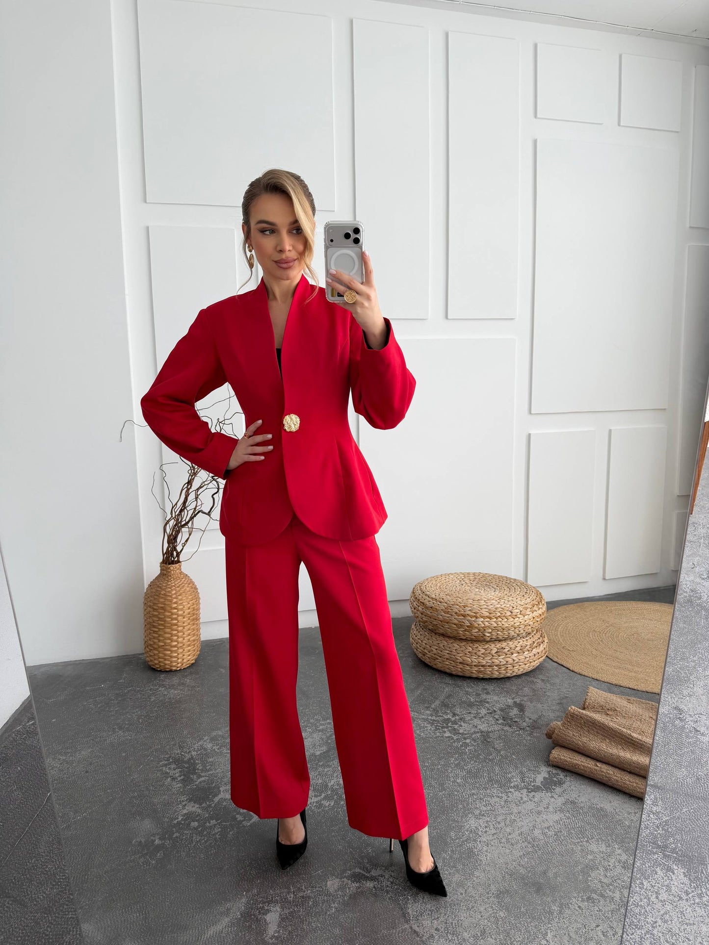 Woman in a red suit taking a mirror selfie in a minimalistic room.