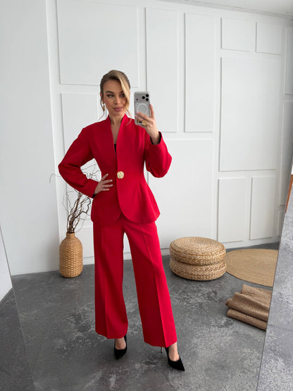 Woman in a red suit taking a mirror selfie in a minimalistic room.