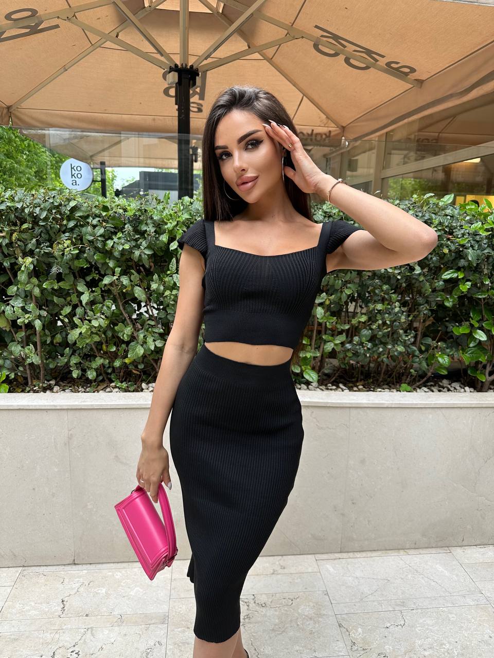 Woman in a black outfit holding a pink clutch outdoors