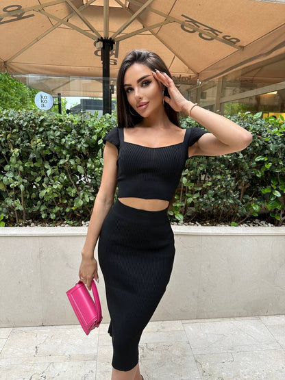 Woman in a black outfit holding a pink clutch outdoors
