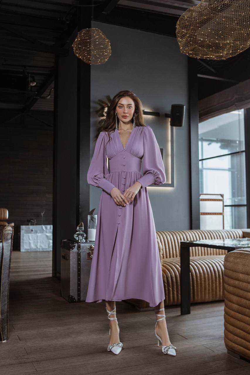 Woman in a lavender dress standing in an elegant interior setting with modern decor.