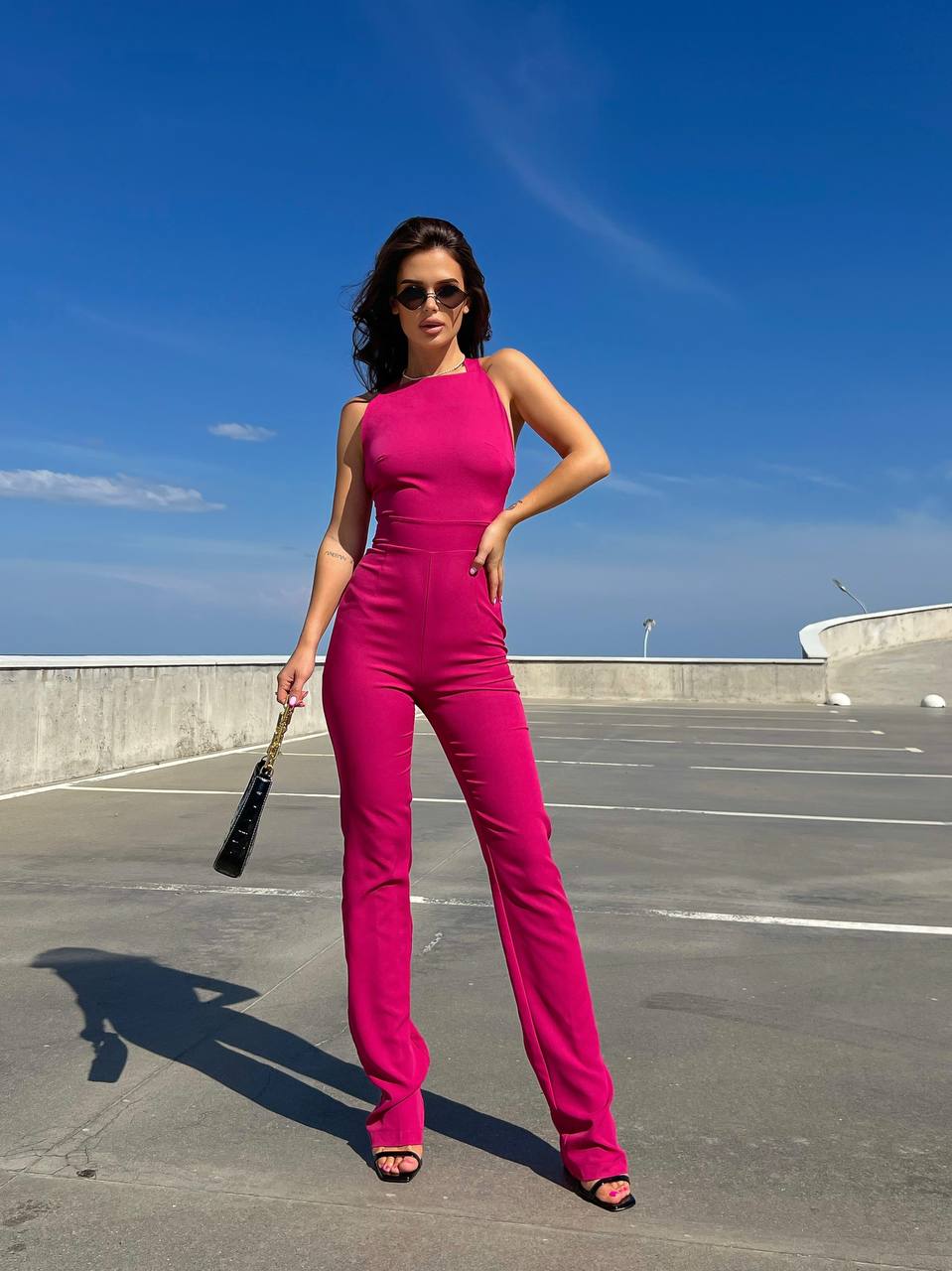 Woman in a bright pink jumpsuit standing on a rooftop with a clear blue sky.
