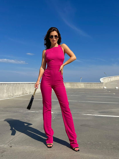 Woman in a bright pink jumpsuit standing on a rooftop with a clear blue sky.