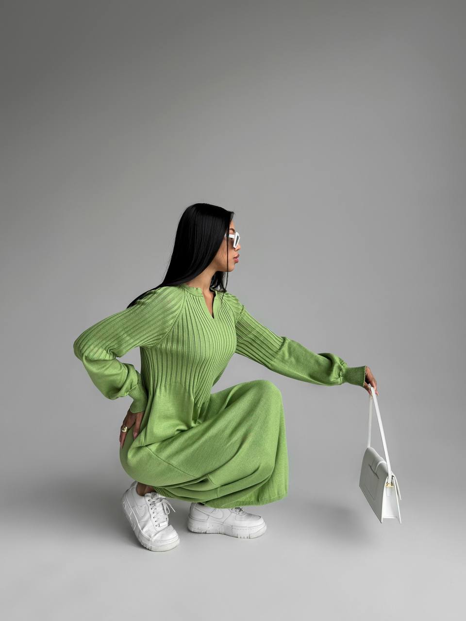 Woman in a green dress holding a white handbag against a gray background