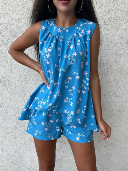 Woman wearing a blue floral sleeveless top and shorts set against a gray background