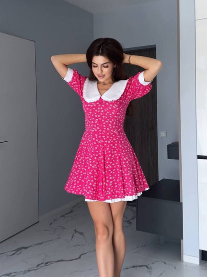 Woman wearing a pink dress with white polka dots and collar in a minimalistic room.