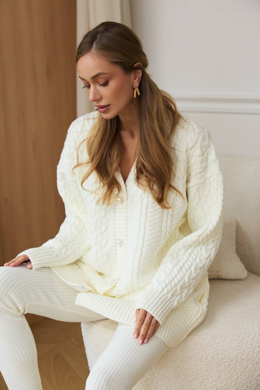 Woman wearing a white cable knit sweater sitting on a couch.