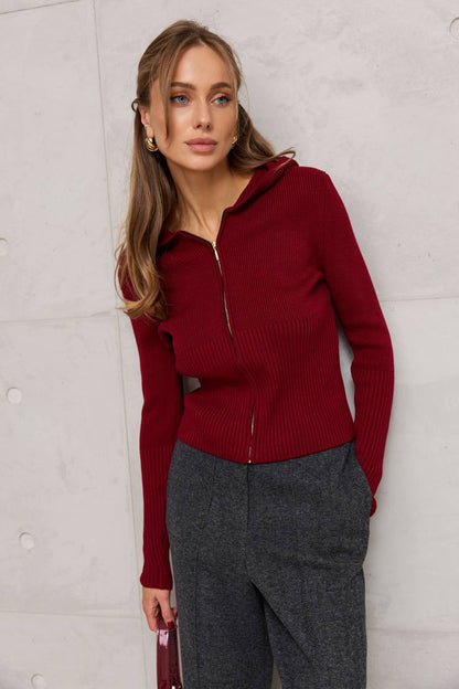 Woman wearing a red zip-up sweater and gray pants against a light gray background