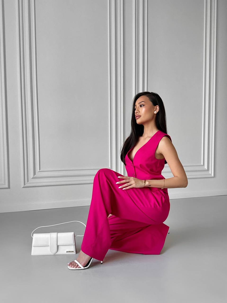 Woman in a bright pink dress sitting on the floor against a gray wall.