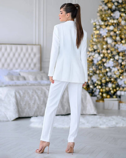 Woman in a white suit standing in a room with a decorated Christmas tree.