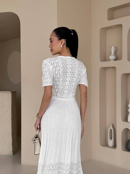 Woman in a white lace dress standing in a minimalistic room with geometric wall designs.