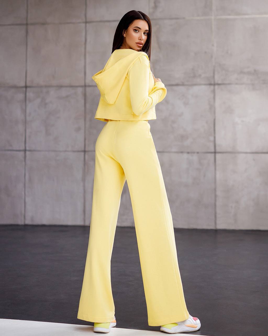 Woman wearing a yellow outfit standing against a gray wall.