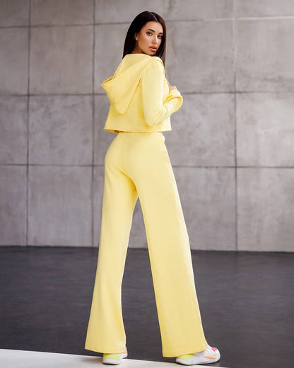 Woman wearing a yellow outfit standing against a gray wall.