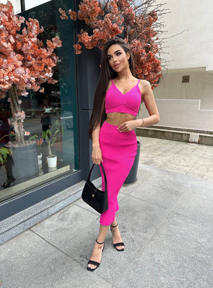 Woman in a bright pink outfit standing outdoors near a building entrance.