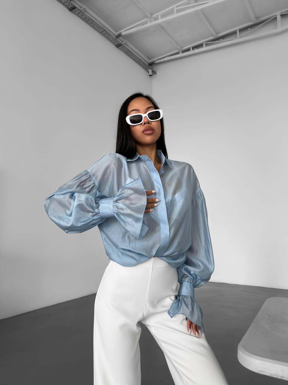 Person wearing a light blue blouse and white pants in a minimalistic setting