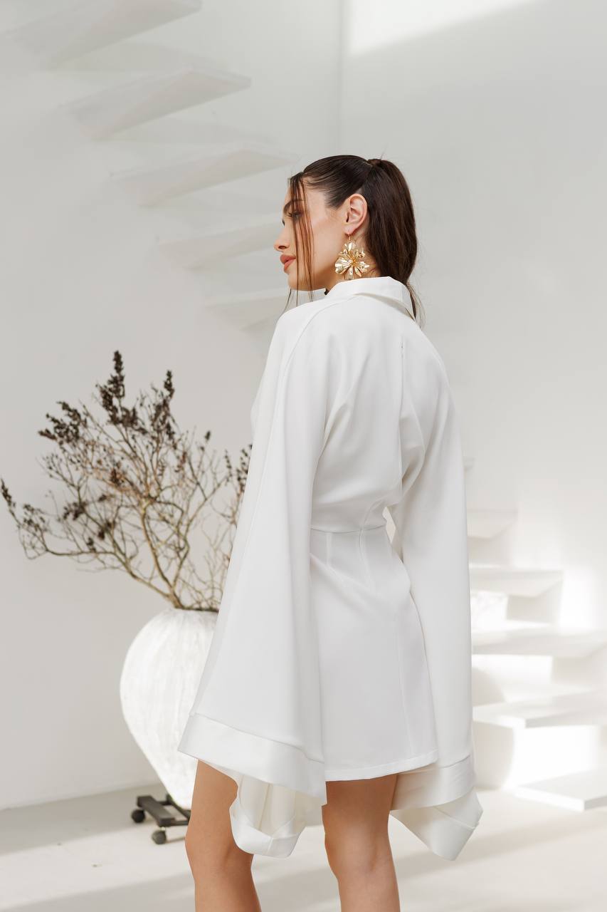 Woman wearing a white shirt in a minimalistic room with a plant.