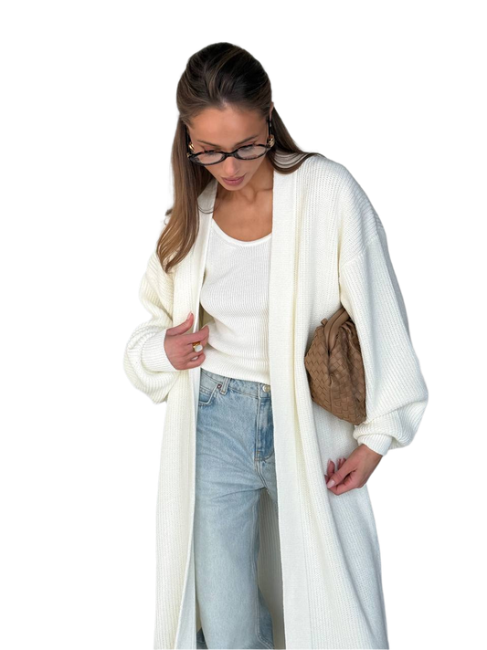 Woman wearing a long cream cardigan over a white top and blue jeans, holding a brown bag on a white background.