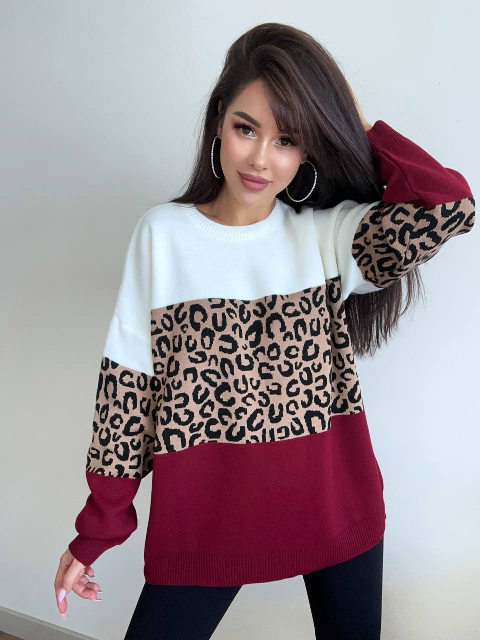 Woman wearing a sweater with leopard print and maroon design against a plain background