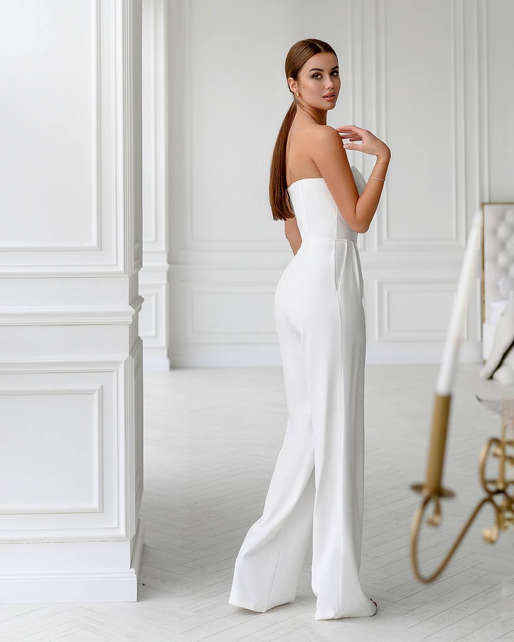 Woman wearing a white strapless jumpsuit in a room with white walls and decor.