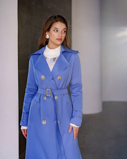 Woman wearing a blue trench coat with gold buttons in an indoor setting
