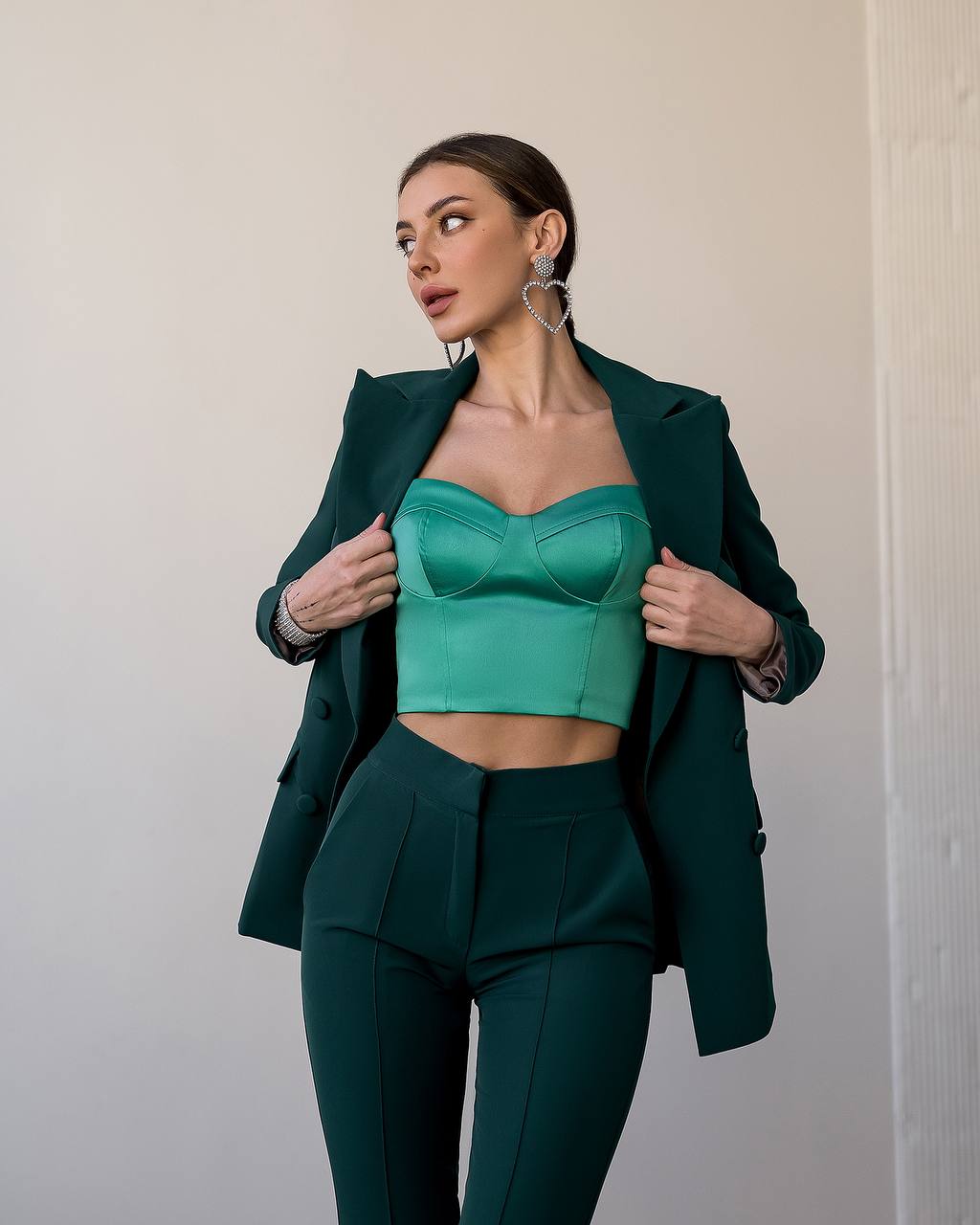 Woman wearing a green outfit with a blazer and top against a neutral background
