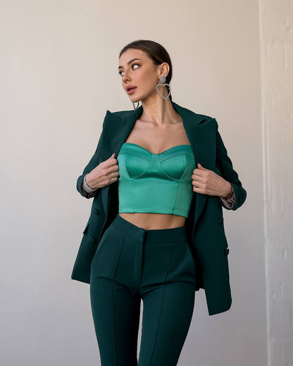 Woman wearing a green outfit with a blazer and top against a neutral background
