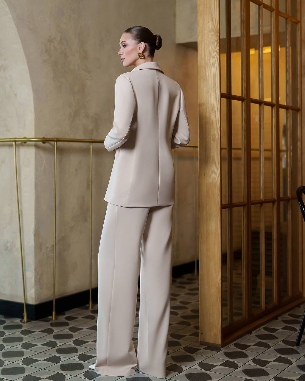 Woman in a beige suit standing in an elegant interior setting.