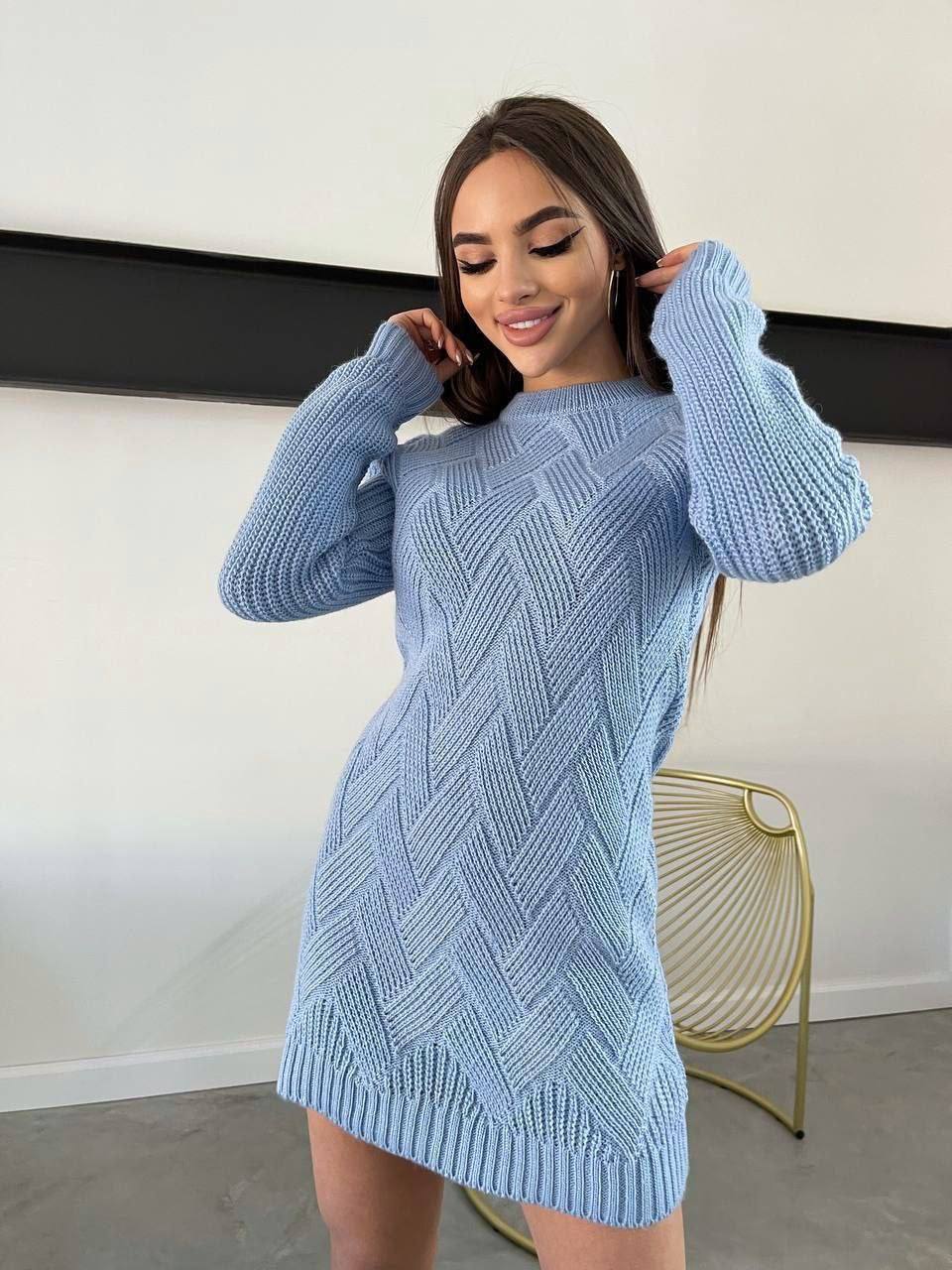 Woman wearing a light blue knitted dress against a white wall.