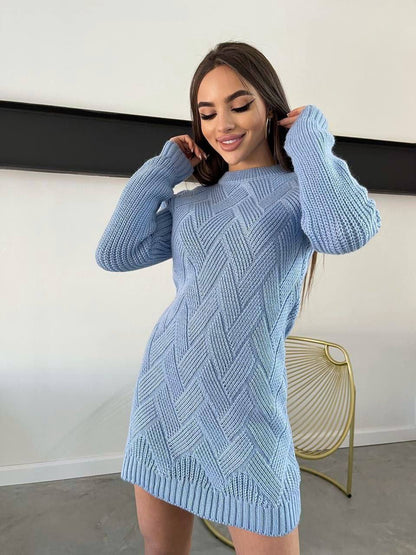 Woman wearing a light blue knitted dress against a white wall.