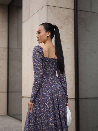 Woman in a floral dress standing against a neutral wall