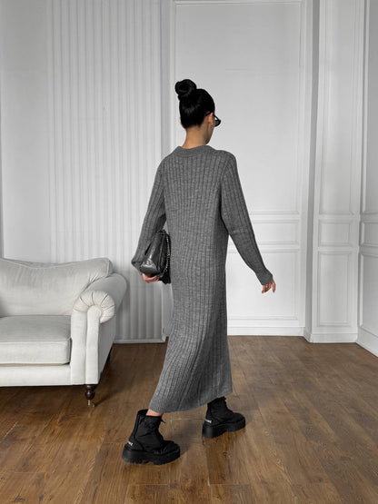 Woman in a gray dress standing in a room with white walls and a gray sofa.