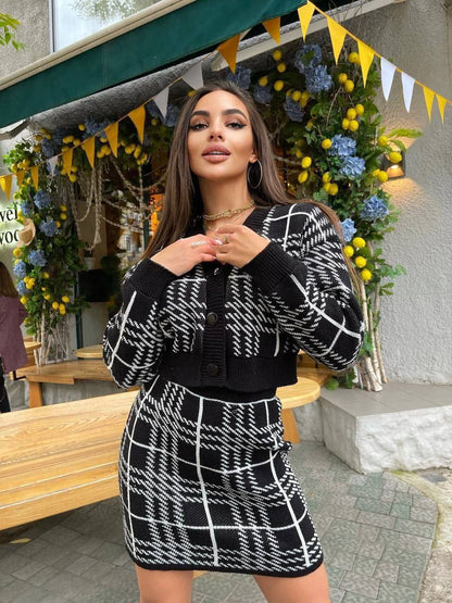 Woman in a black and white checkered outfit standing in front of decorative plants and flags.