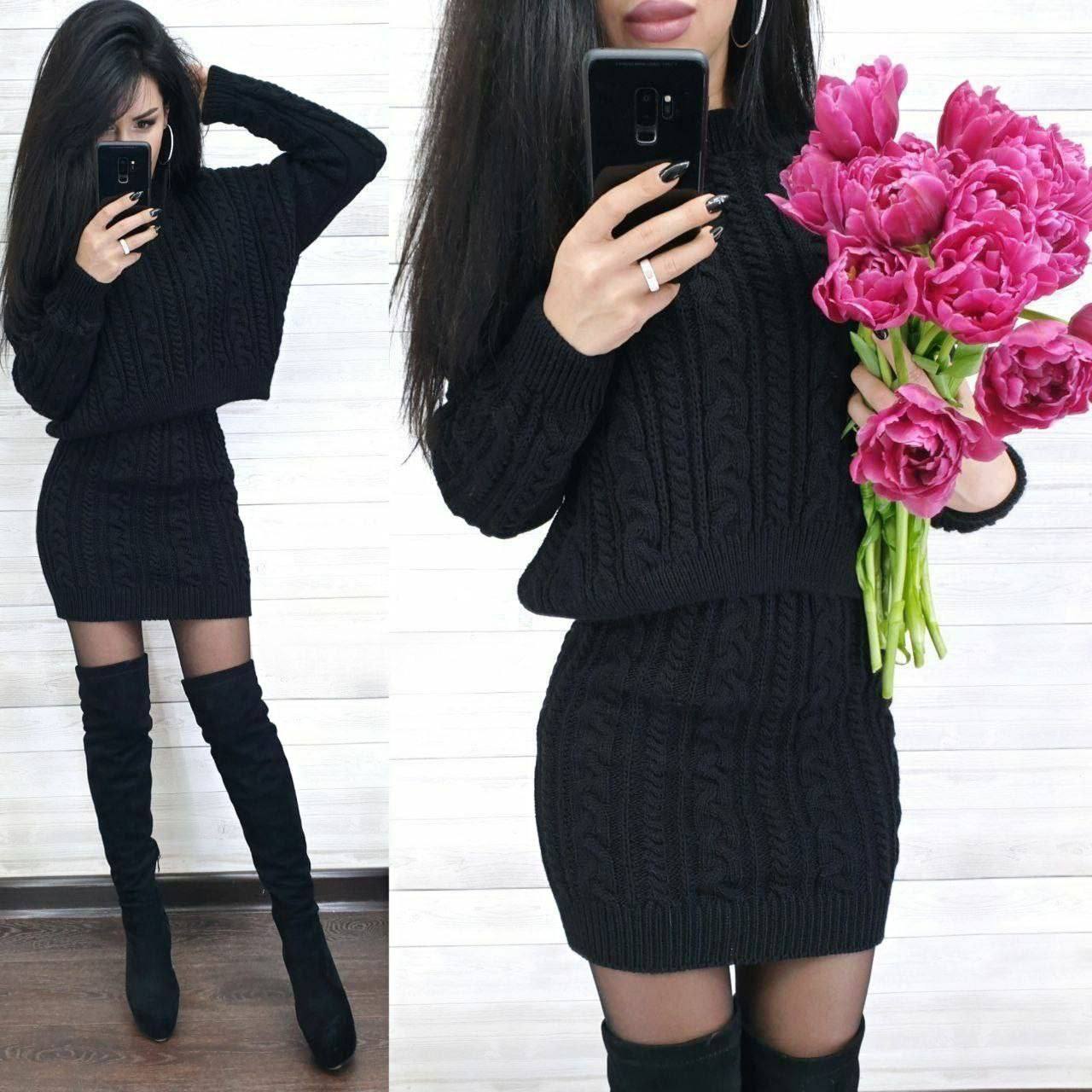 Woman wearing a black cable knit dress with knee-high boots, holding pink flowers.